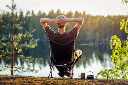 Man sitting on camp chair by lake by PEO Canada
