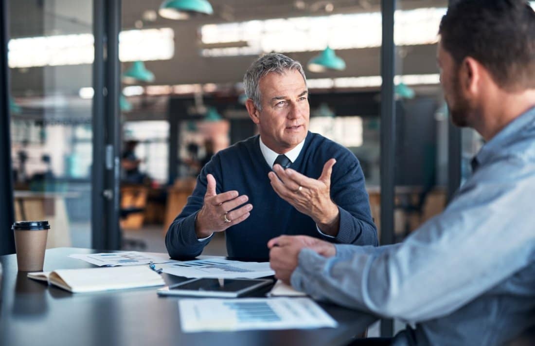 Two Men Engaged in Conversation at a Table within a Professional Office at PEO Canada