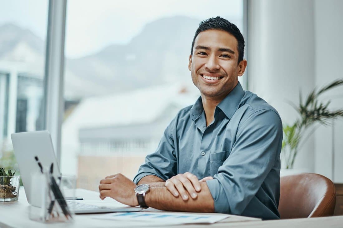 A Smiling Man Seated at a Desk, Engaged with his Laptop in North America 